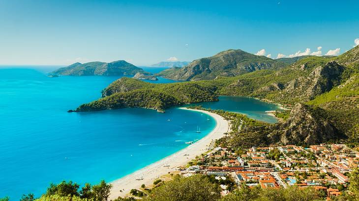 A beach town next to a sandy shore, turquoise ocean, and greenery-covered hills