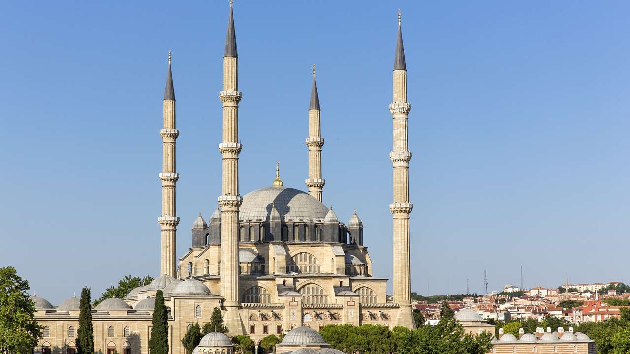 A large mosque with a dome and minarets next to trees and a blue sky