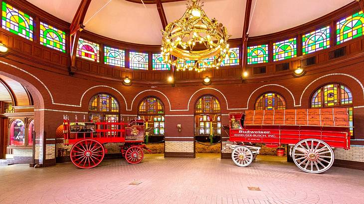 Antique red wagons against a brown wall with arched doors under a chandelier