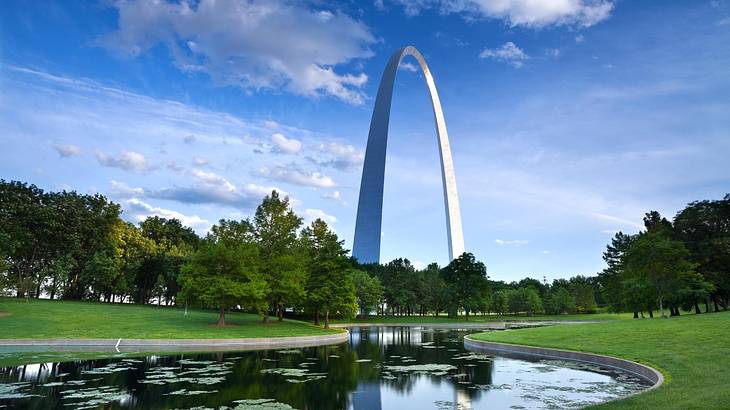 A huge arched monument overlooking a pond winding through green grass A huge arched monument overlooking a pond winding through green grass