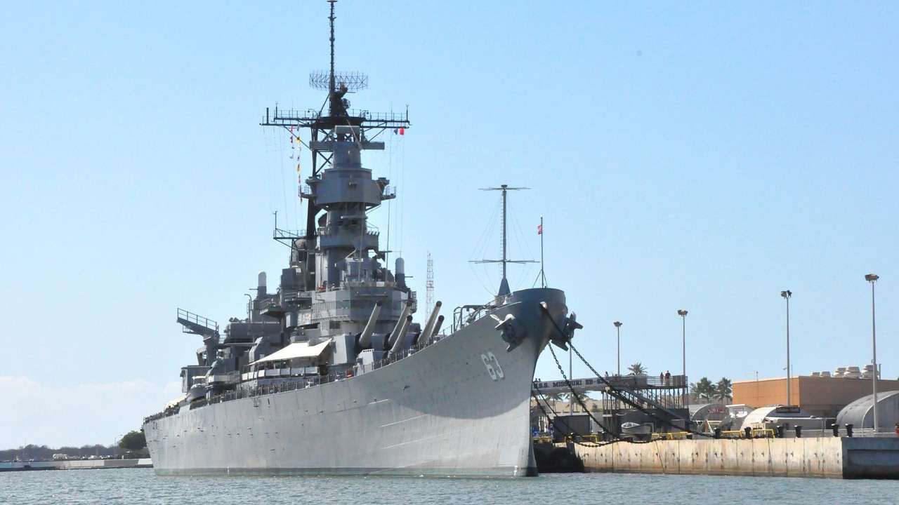 A gray battleship docked at a port under a clear blue sky