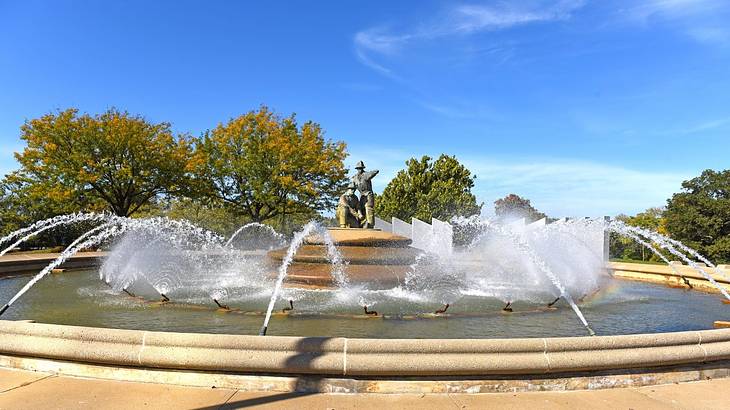 A round fountain with a statue of a firefighter in the middle, against some trees A round fountain with a statue of a firefighter in the middle, against some trees