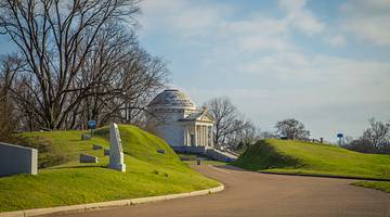 A white dome in the middle of a park surrounded by green hills and leafless trees