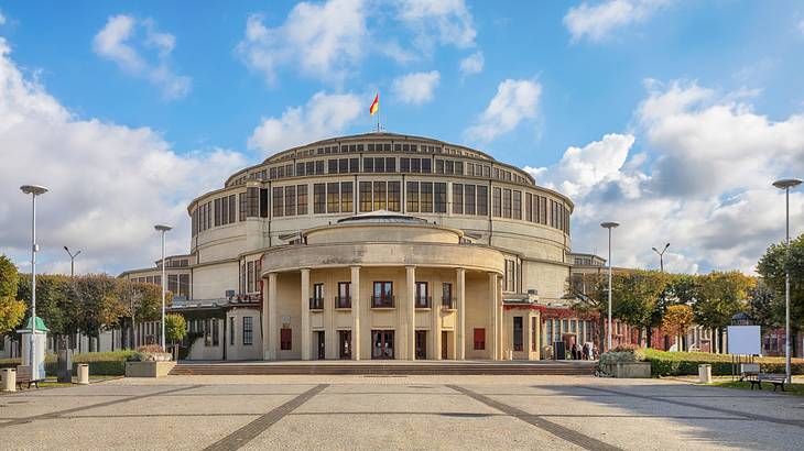 A large building with a dome, columns, and a flag on top under a blue sky with clouds