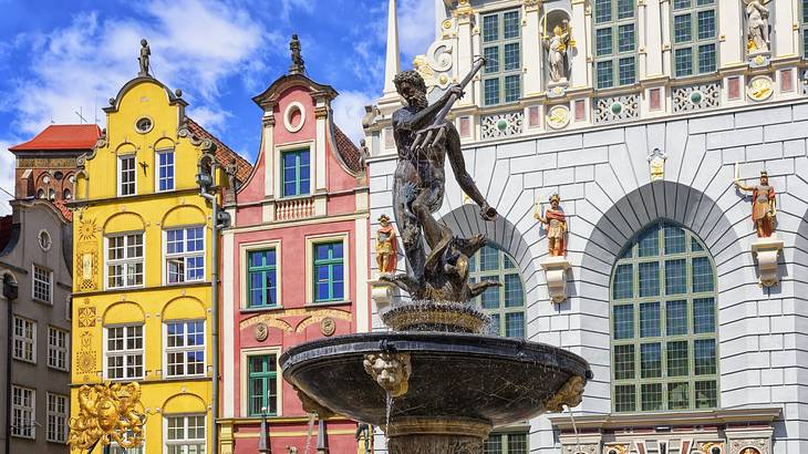 A statue of Neptune on a fountain next to colourful buildings