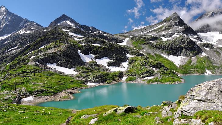 A view of a glacial lake next to greenery and mountains with snow on them