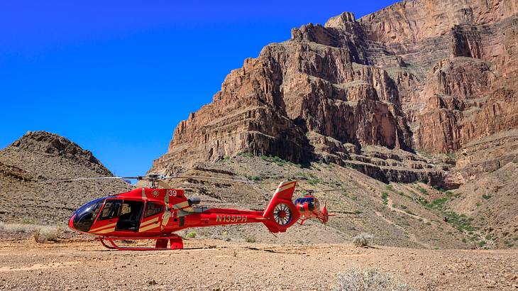 A red helicopter in the desert surrounded by high brown rocks