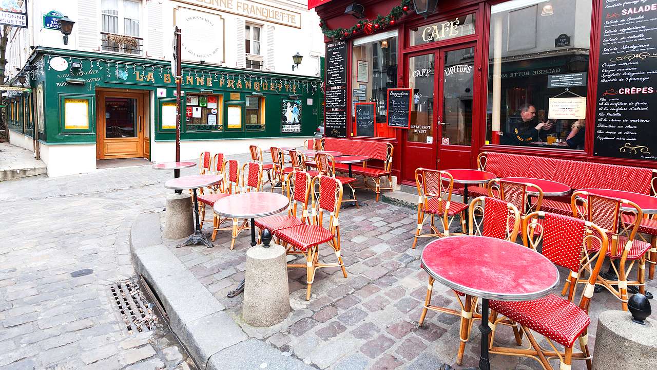 A cafe restaurant with red tables and chairs arranged along a street corner