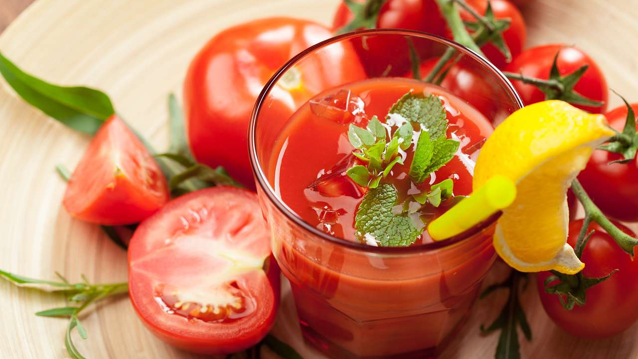 A glass of tomato juice with herbs and a lemon on top, surrounded by tomatoes