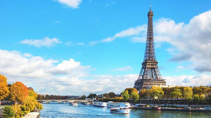 A tall grey tower with a pointy top across a river on a sunny day