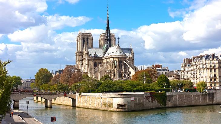 A gothic church surrounded by trees overlooking a body of water under a sunny sky