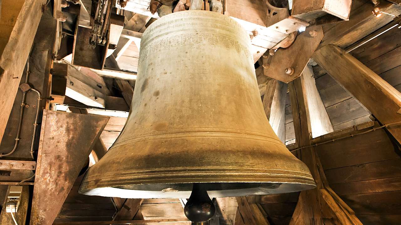 A huge, metal bell surrounded by a wooden interior and beams