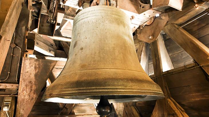 A huge, metal bell surrounded by a wooden interior and beams