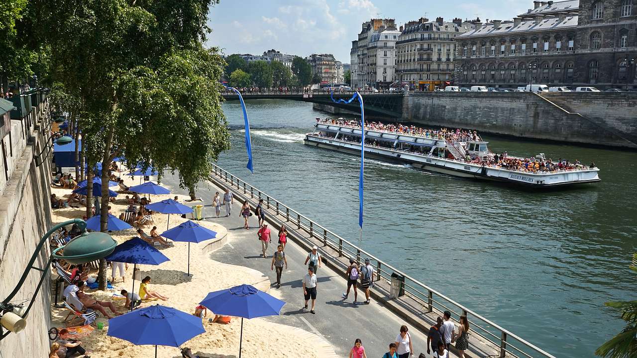 People enjoying the artificial beach along the tree-lined bank of a river with a boat