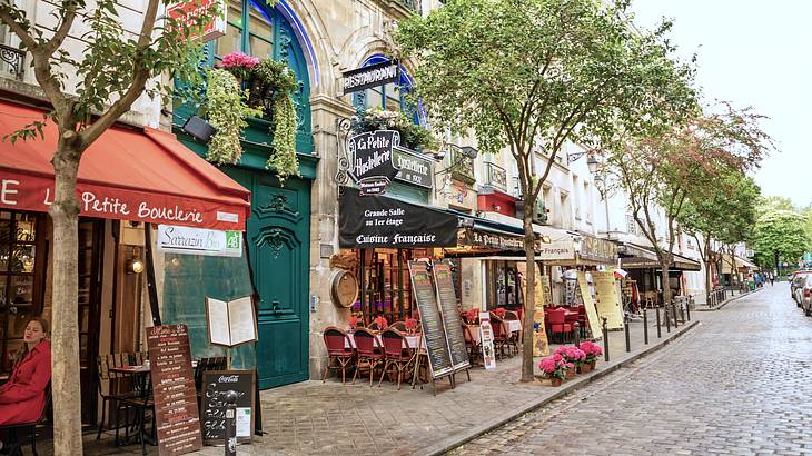 A cobbled street lined with buildings, cafes, and trees