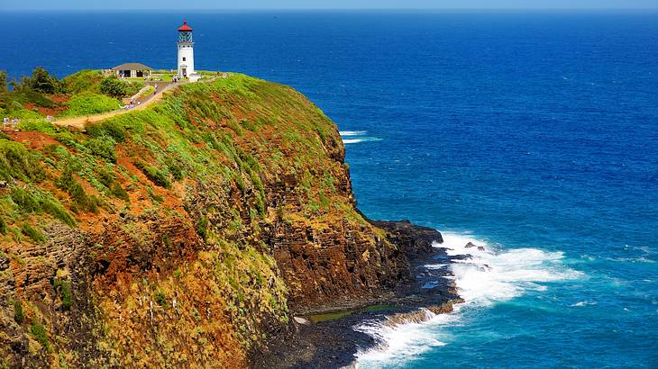 A lighthouse on top of a dramatic backdrop of cliffs plunging into the ocean