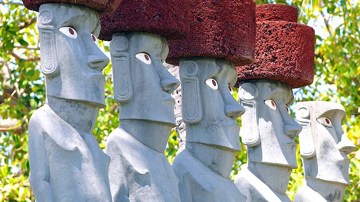 A row of stone statues with red headpieces on a sunny day