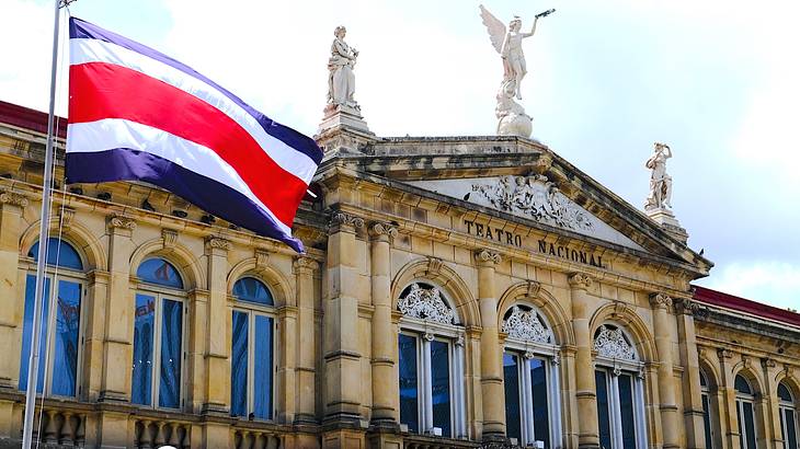 Red, white and blue striped flag waving in the wind in front of a yellow building