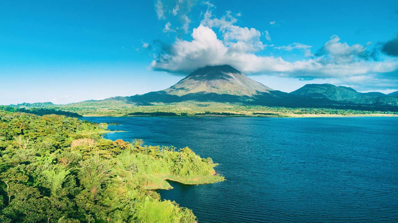 View of a volcano from behind a lake, rising from a rainforest