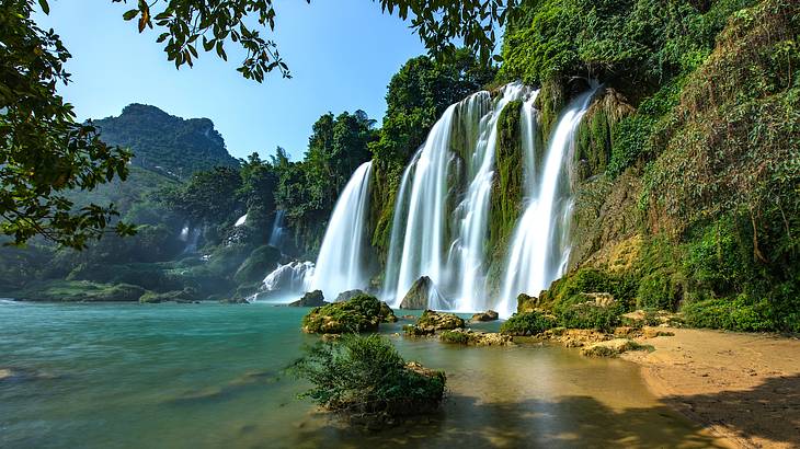 A waterfall going off a lush green cliff with mountains and trees around it