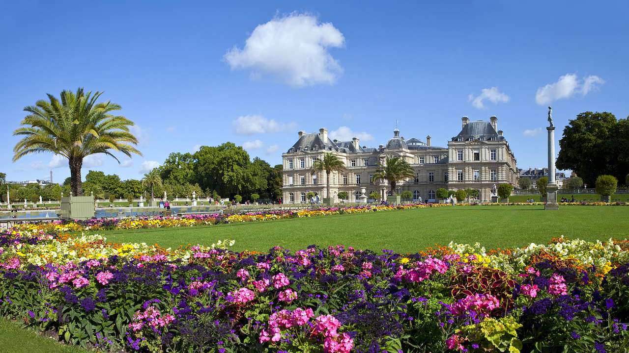 Colourful flowers, a green lawn and a statue, with Luxembourg Palace seen from afar