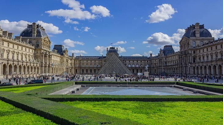 Louvre Pyramid at the front of the Louvre Museum with people passing by