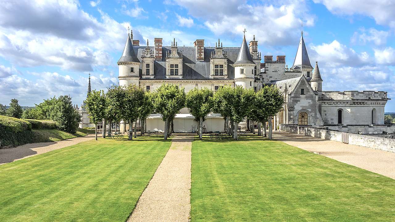 Château Royal d'Amboise under a cloudy blue sky facing trees and a manicured lawn