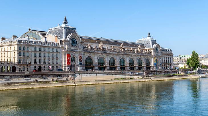 Side view of Musée d'Orsay facing a river next to trees and other buildings