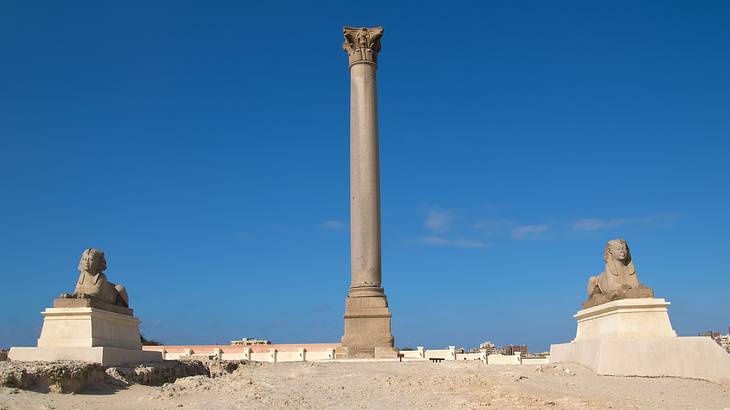 A pillar standing in the middle of two sphinx against a blue sky A pillar standing in the middle of two sphinx against a blue sky