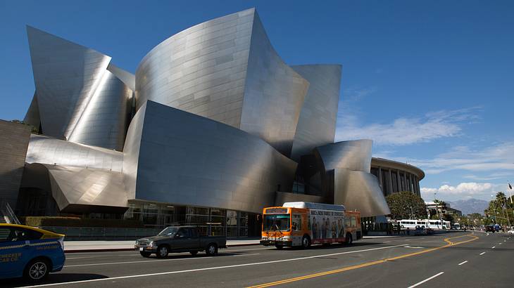 A silver futuristic-looking building along a street with cars going by on a nice day