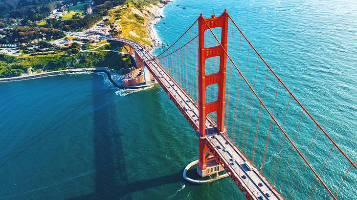 Aerial of a long red bridge over water, ending on a coastline with greenery