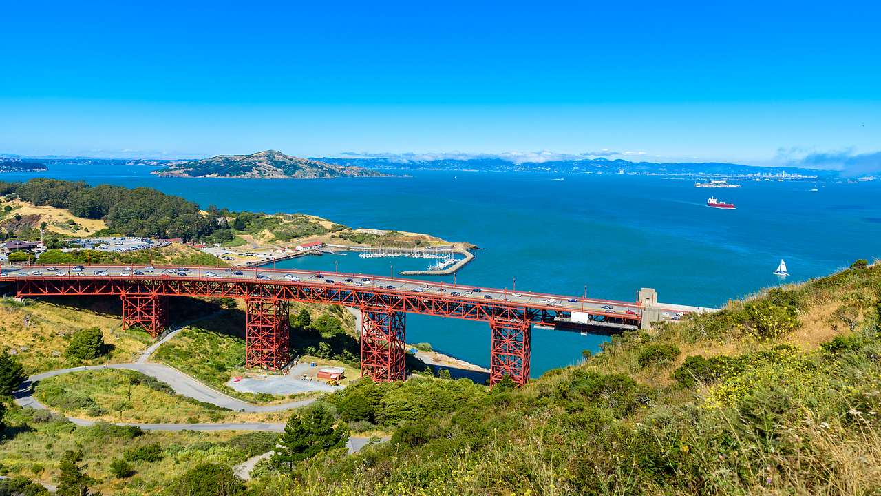 A red bridge over mountainous land covered in greenery with the sea at the back