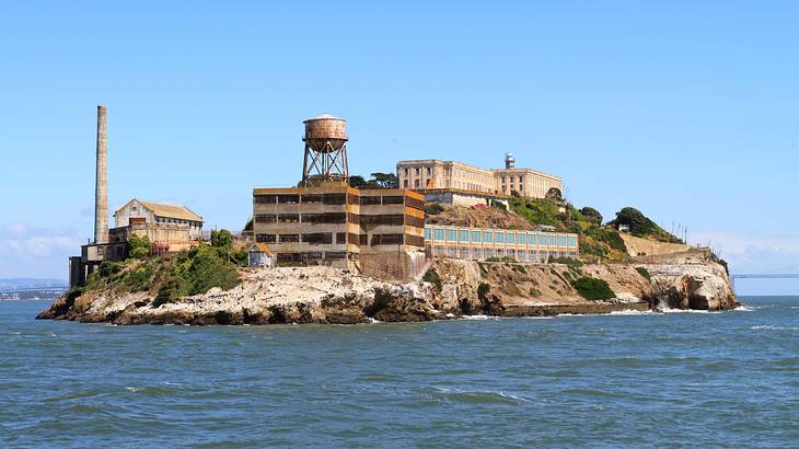 A small hilly island with structures, surrounded by ocean and mountains in the back