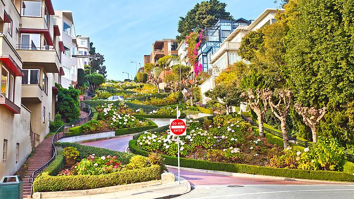 A steep, zigzagging street with plants and colorful flowers in between buildings
