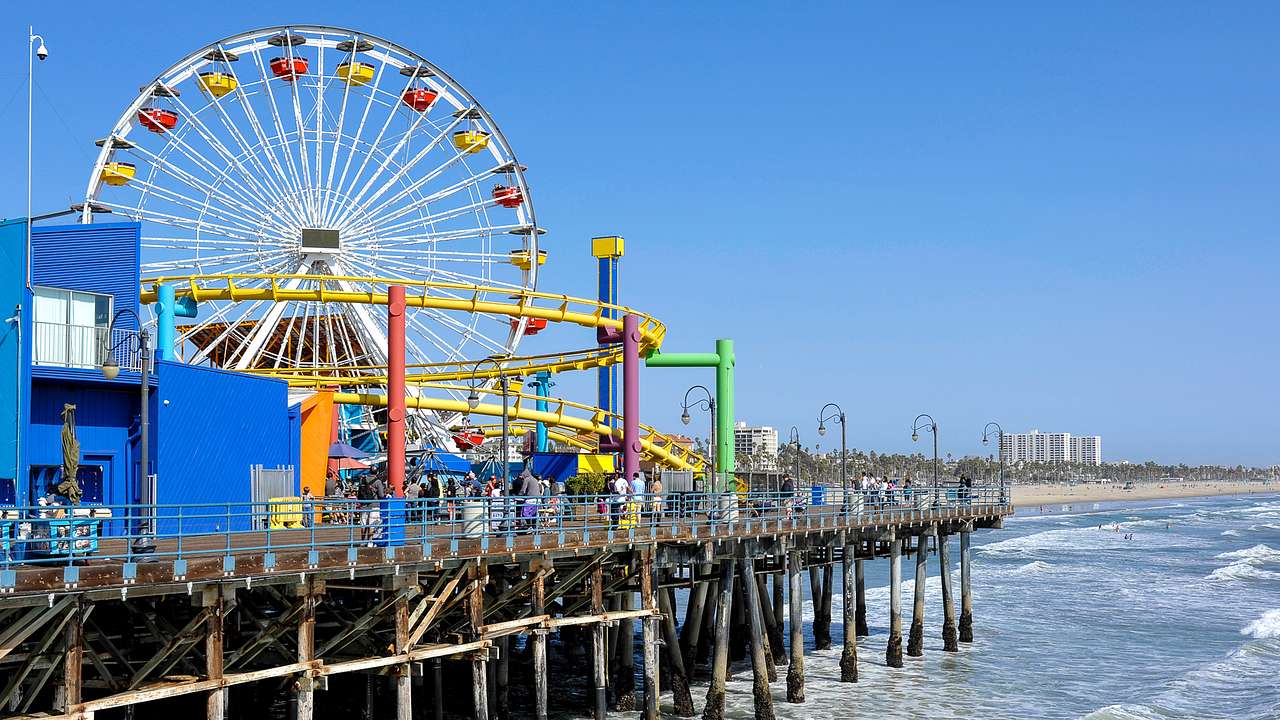 A wooden pier with a colorful amusement park with a Ferris wheel facing the ocean