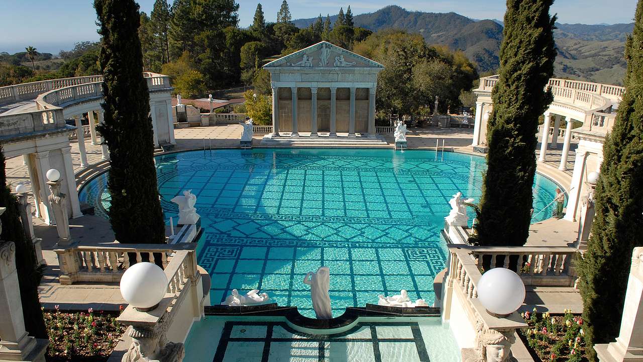 A luxurious Roman-style pool with graphic tiles and white statues surrounding it