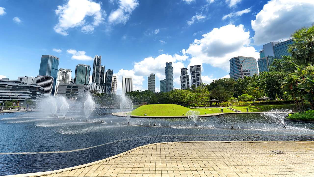 A public park with a skyline full of buildings behind and a wide water fountain