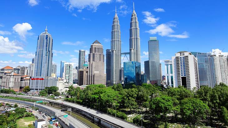 A twin-tower building surrounded by tall buildings facing skyway roads next to trees