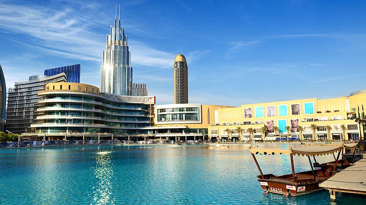 A glass mall surrounded by other tall buildings and water in front