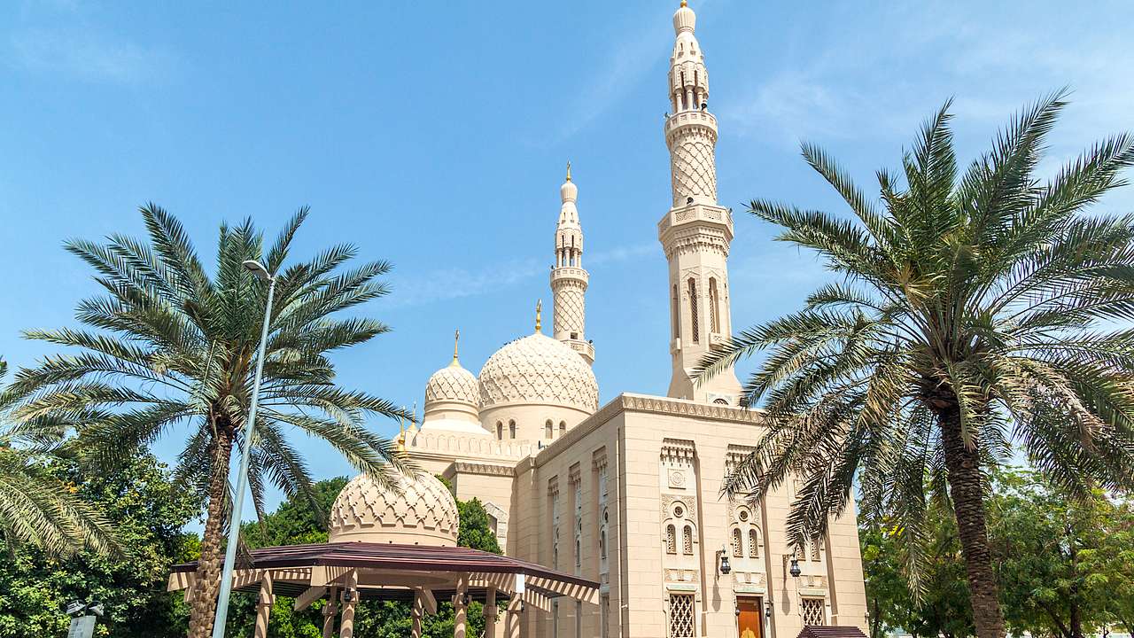 A traditional mosque with two towers and a white stone exterior facing palm trees