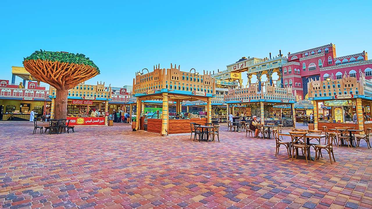 A colorful courtyard with tables and chairs and stalls in the background