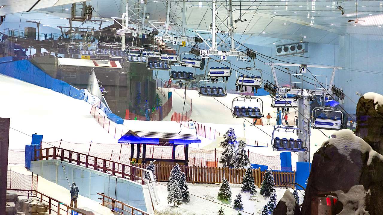 An indoor snowfield with trees, ski slopes, and empty cable cars