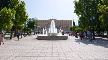 A courtyard with trees on both sides and a big building in the back facing a fountain