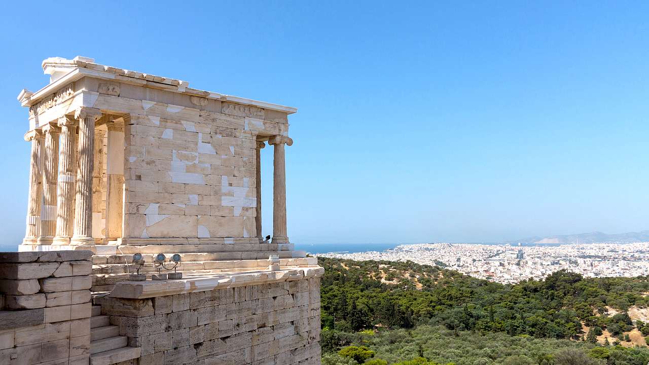 An intricate temple on a hill overlooking the city buildings in Athens