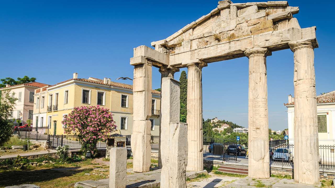 An ancient gate made of columns next to city buildings on a sunny day