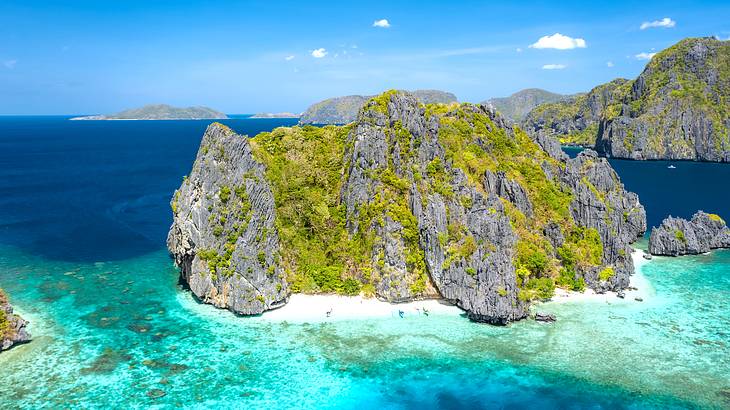 Blue sea with rocky cliffs with greenery, and other islands in the distance