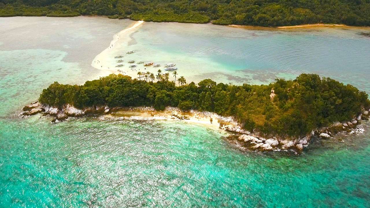 Aerial shot of a lush island connected to another island by a white sand bar