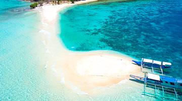 Aerial view of a white sand beach surrounded by pristine, blue water, with two boats