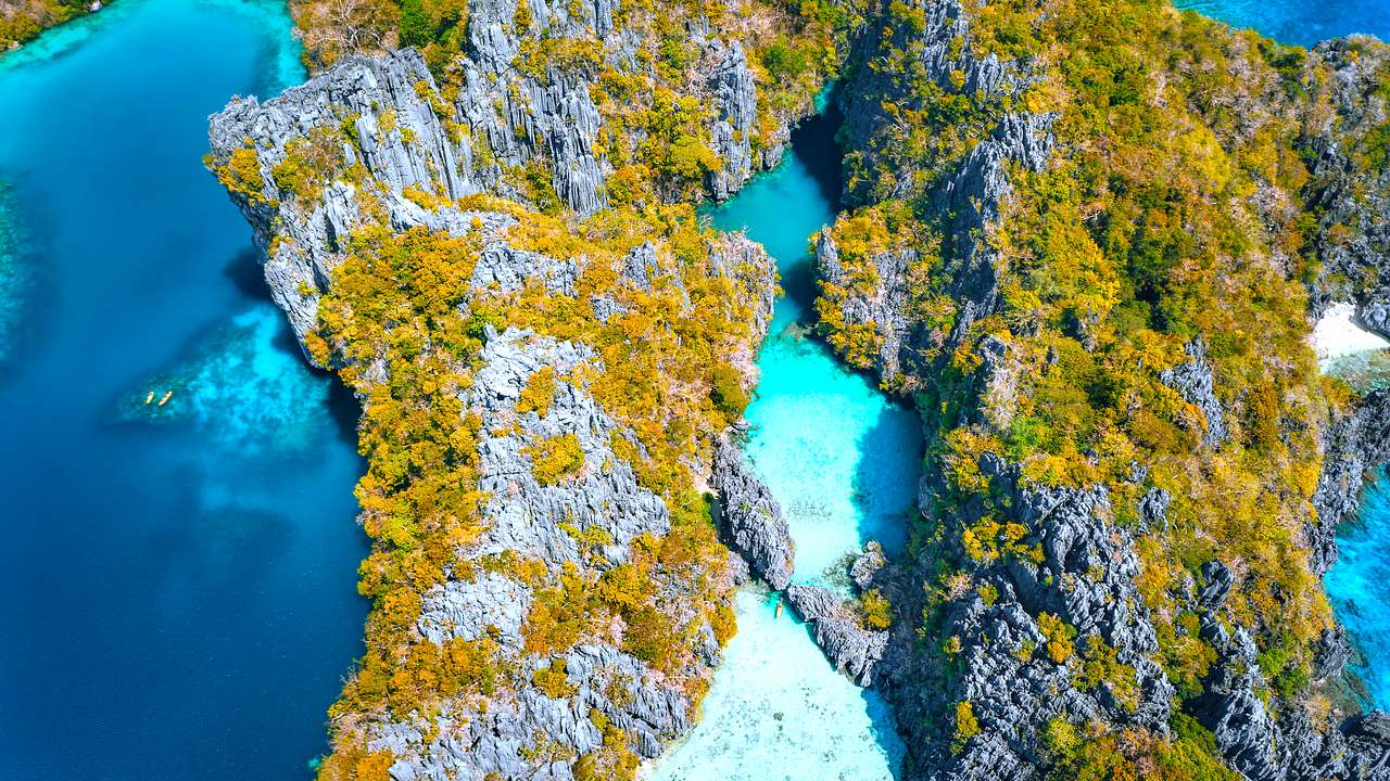 A small, blue lagoon from above surrounded by rocky cliffs with patches of greenery