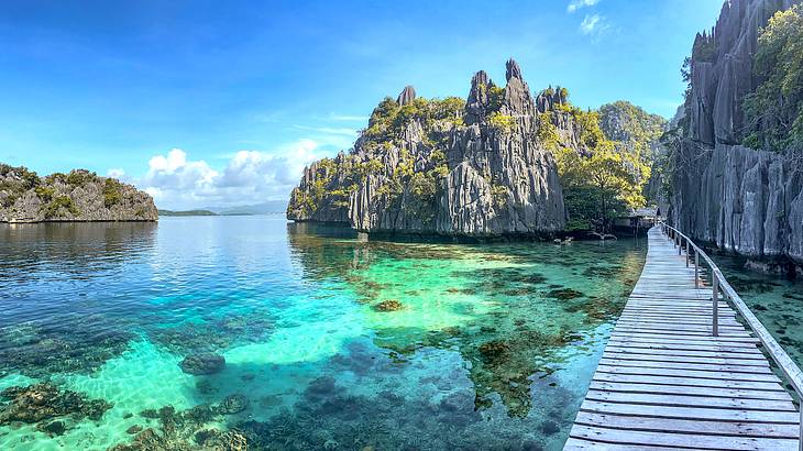 A wooden boardwalk around a lagoon full of clear blue water and limestone cliffs